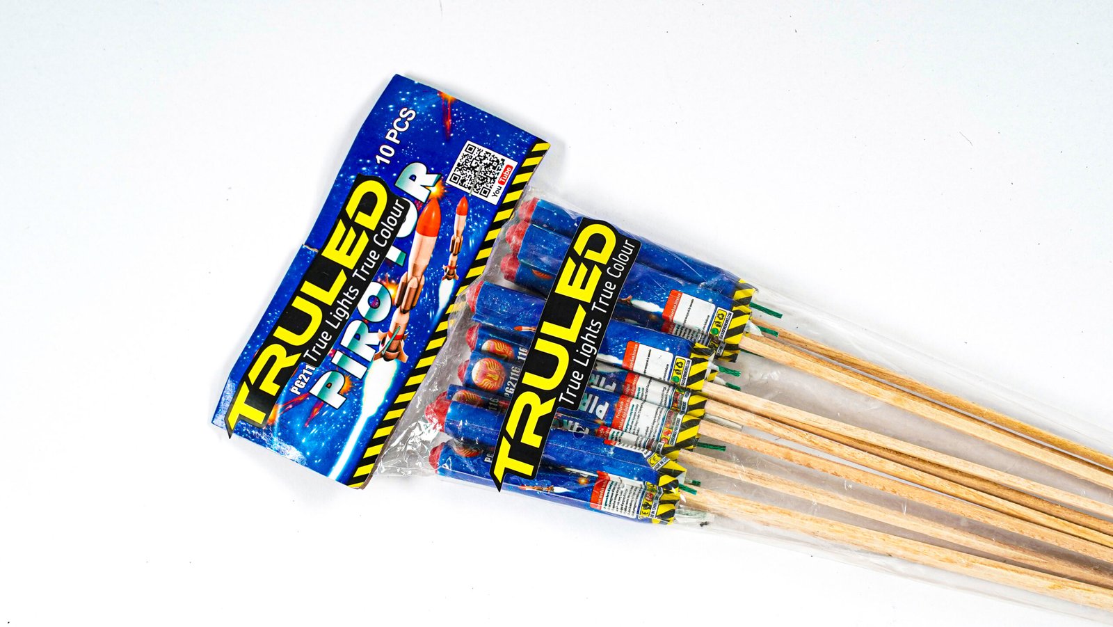 Boxed fireworks labeled "True Colours" with blue space design and 10 pieces, alongside separate rocket tubes and wooden sticks ready for use.